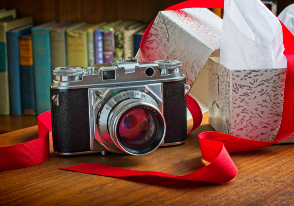 Vintage film camera with red ribbon on wooden table beside gift box and books, perfect for beginner photography inspiration